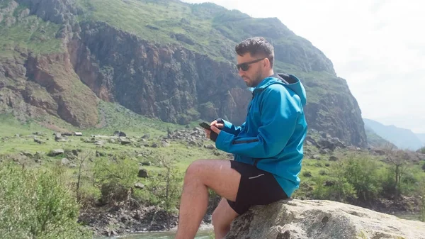 Un hombre con gafas se sienta en el borde de un acantilado con un anorak azul. Cañón Katu-Yaryk Valle Chulyshman. Altai. —  Fotos de Stock