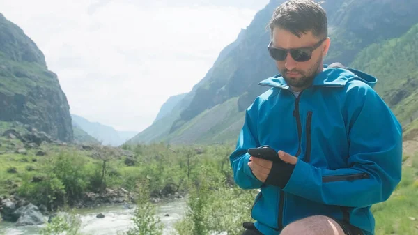 Un hombre con gafas se sienta en el borde de un acantilado con un anorak azul. Cañón Katu-Yaryk Valle Chulyshman. Altai. —  Fotos de Stock