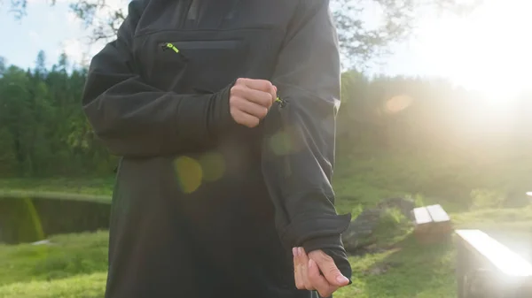 Una chica con gafas abre el bolsillo de un anorak gris sobre el fondo de un paisaje — Foto de Stock