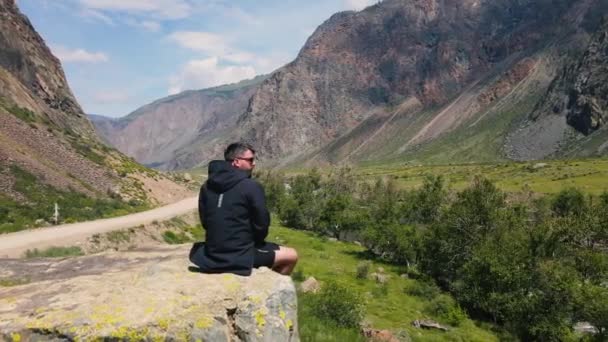 Uçurumun kenarında oturan bir adam siyah bir anorak giyiyor. Katu-Yaryk Kanyonu Chulyshman Vadisi. Altai. — Stok video