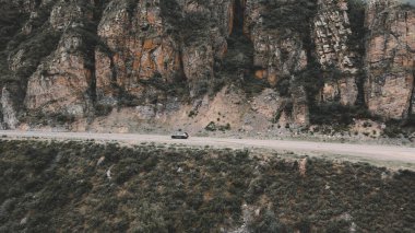 Dağlardaki dar yollardan koyu gri bir araba geçiyor. İnsansız hava aracı görüntüleri