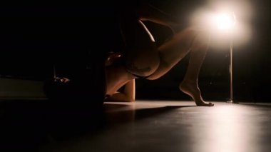 Sert ışıklandırma yapan seksi bir kadın bacaklarını ve kemerlerini sırtına kaldırıyor. Siyah arkaplan.