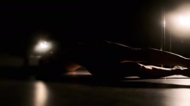 Sert ışıklandırma yapan seksi bir kadın bacaklarını ve kemerlerini sırtına kaldırıyor. Siyah arkaplan.