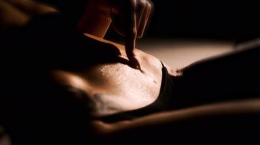 Kız parmağını bir damla suyla çıplak karnının üzerinde gezdiriyor. Sert ışık, siyah arka plan. Yakın plan.