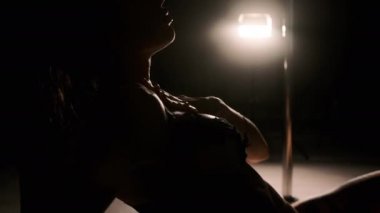 Kız parmağını bir damla suyla çıplak karnının üzerinde gezdiriyor. Sert ışık, siyah arka plan. Yakın plan.