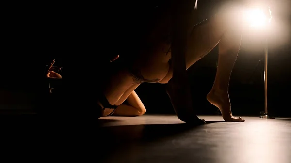 Μια σέξι γυναίκα με σκληρό φωτισμό σηκώνει τα πόδια και τις καμάρες της στην πλάτη. Μαύρο φόντο. — Φωτογραφία Αρχείου