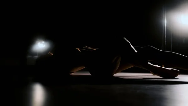 Eine sexy Frau in grellem Licht hebt ihre Beine und wölbt sich in ihrem Rücken. Schwarzer Hintergrund. — Stockfoto