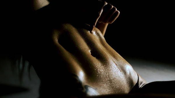 Το κορίτσι τρέχει το δάχτυλό της πάνω από το γυμνό στομάχι της με σταγόνες νερού. Σκληρό φως, μαύρο φόντο. Κοντινό πλάνο — Φωτογραφία Αρχείου