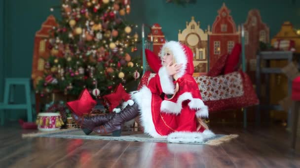 Χαριτωμένο κορίτσι cosplaying Χριστούγεννα Miku Σάντα φόρεμα με δώρα. Το ξωτικό της Πρωτοχρονιάς. Κάθεται στο πάτωμα, ισιώνει τα μαλλιά της — Αρχείο Βίντεο
