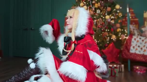 Linda chica cosplaying Navidad Miku Santa vestido con regalos. Año Nuevo elfo. Se sienta en el suelo — Vídeos de Stock