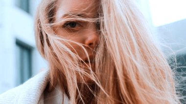 Beyaz önlüklü ve eşarplı bir kız onun kalın saçlarını düzeltir. Güçlü rüzgar. Arka planda iş merkezi var. Başarı