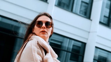 Şehrin iş bölgesinde bej ceketli ve gözlüklü bir kız caddede yürüyor, güçlü bir rüzgar var. Başarı