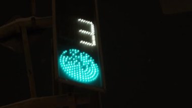 Trafik ışığı yeşili geri sayıyor. Kırmızı ışık yanıyor. Gece kıştır. Kar yağıyor.