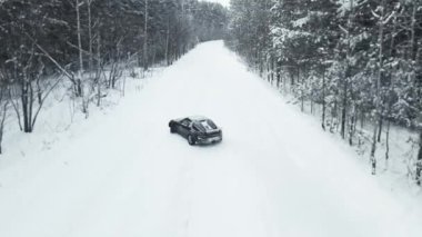 MOSCOW, RUSSIA - 13 DECEMBER 2020: Black luxury sports car is drifting in a snowy forest in winter. Drone view