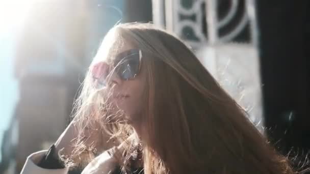 Portrait of a girl with glasses in the bright sun, a busy city on the background. Close-up, fashion — Stockvideo