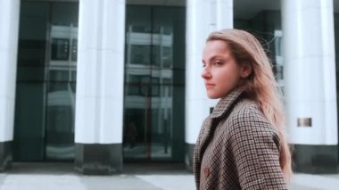 Paltolu bir kız gülümseyerek caddede yürüyor. Arka planda iş merkezi var. Başarı