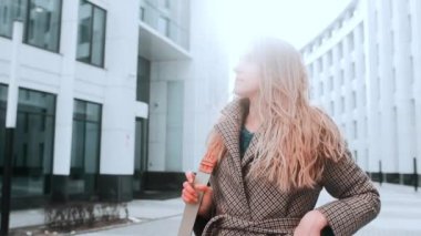 Paltolu bir kız gülümseyerek caddede yürüyor. Arka planda iş merkezi var. Başarı