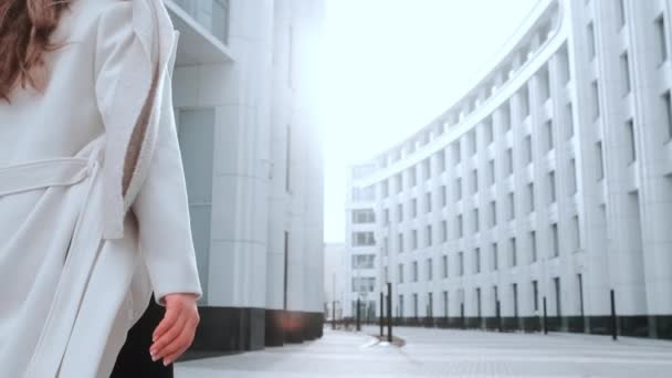 Dziewczyna w białym płaszczu i szaliku idzie ulicą, uśmiechnięta. Centrum biznesowe w tle. Sukces — Wideo stockowe