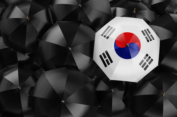 Umbrella with South Korean flag among black umbrellas, top view. 3D rendering