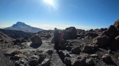 Kampa giderken büyük bir kayanın üzerinde küçük sevimli bir kardan adam. Sırt çantalı siyah bir adam dağ yolunda yürüyor. Mawenzi Dağı. Dağ manzarası. Kilimanjaro 'ya tırmanmak.