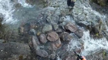 Taşların üzerinde küçük bir dağ nehrini geçmek. Birinci şahıs görüşü. Dağlarda küçük bir şelale. Tırmanan Kilimanjaro, Tanzanya, Afrika.