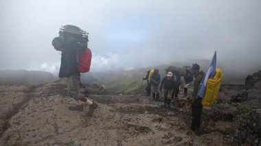 Kilimanjaro, Tanzanya - 30 Aralık 2021: Bir grup turist, rehber ve hamal dağa tırmanıyor. Sisli dağ manzarası. Kilimanjaro 'ya tırmanmak.
