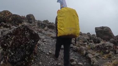 Büyük bir sırt çantası olan bir adam sisli dağlık bir alanda, kayaların ve kayaların yanından geçiyor. Dağ manzarası. Tırmanan Kilimanjaro, Tanzanya, Afrika.