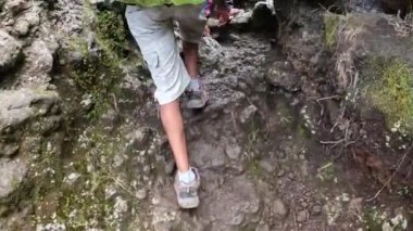 Büyük bir sırt çantası olan siyah bir adam kayalık bir dağ yoluna tırmanıyor. Arkadan bacaklara bak. Tırmanan Kilimanjaro, Tanzanya, Afrika.