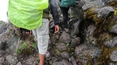 Kilimanjaro, Tanzanya - 30 Aralık 2021: Büyük sırt çantalı siyah bir adam ekibiyle birlikte tehlikeli ıslak kayalara tırmanıyor. Kilimanjaro 'ya tırmanmak. Dağlara yağmur yağıyor..