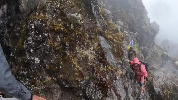 Een Wandelaar Een Regenjas Beklimt Gevaarlijke Vochtige Rotsachtige Stenen Bergop — Stockvideo