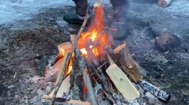 A man puts firewood and logs on a small fire. Yellow-orange flames. Hiking life. Winter hike. Burning branches.