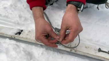 A man fixes a binding on a touring ski. Close-up of hands. Ski trip in the forests of Russia. Straight knot.