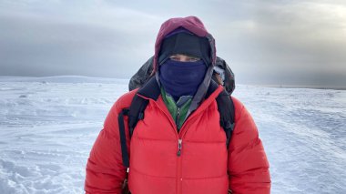 Survival in the north. A man in warm clothes with a backpack behind his back looks at the camera. Close-up on the eyes. Winter hike. Harsh northern nature. Beautiful winter landscape.