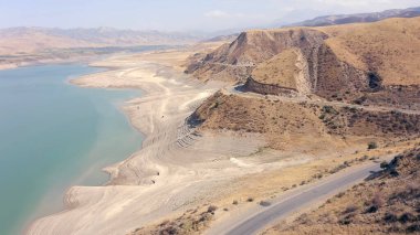 Aerial view of the mountain road near the reservoir. Rocky mountains and slopes of Kyrgyzstan. Amazing natural background. Beautiful summer landscape.