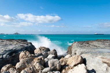 Büyük Bahama adasında aşınmış bir kıyıya vuran dalganın görüntüsü ve arka planda bir kargo gemisiyle ıslak bir rıhtım..