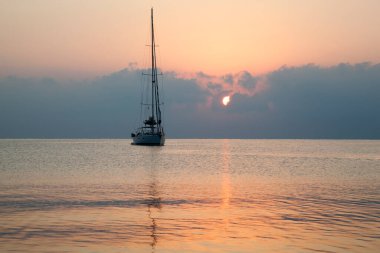 Kemer tatil beldesinde (Türkiye) bulutlu gündoğumu sırasında sürüklenen bir yatın manzarası).