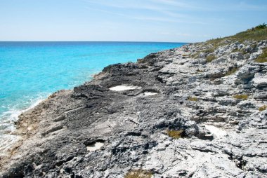 Turkuaz renk sularının manzarası ve ıssız Yarım Ay Cay Adası 'ndaki kayalık bir kıyı şeridi (Bahamalar)).