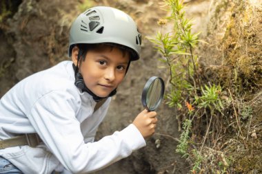 Çocuk büyüteçle bir bitkiyi gözlemliyor.