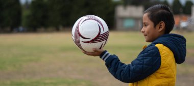 Çocuk oynamak üzere, elinde bir futbol topu tutuyor.