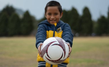 Çocuk oynamak üzere, elinde bir futbol topu tutuyor.
