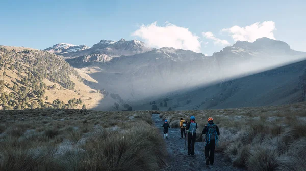 Bir grup yürüyüşçü arka planda dağlarla çayırlarda yürüyor.