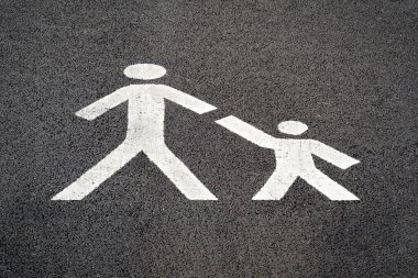 Parent child pedestrian road sign, white paint on tarmac, indicating a safe place for families to cross a carpark road towards a busy shopping centre. 