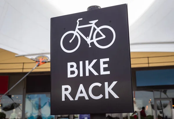 Large black and white bike rack parking sign close up indicating a safe place to park your bicycle in busy urban shopping street area.