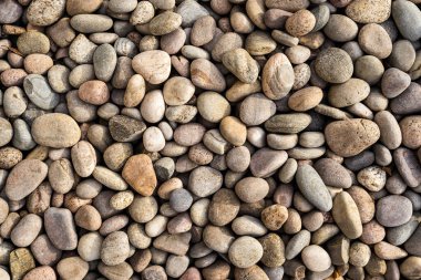 Abstract close up of multicoloured smooth round natural tone stones and pebbles on a beach. 