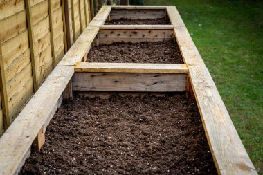 Arka bahçedeki büyük ahşap sebze kutularını kapatın. Tohum ve sebze ekmeye hazır taze organik toprakla doldurun..