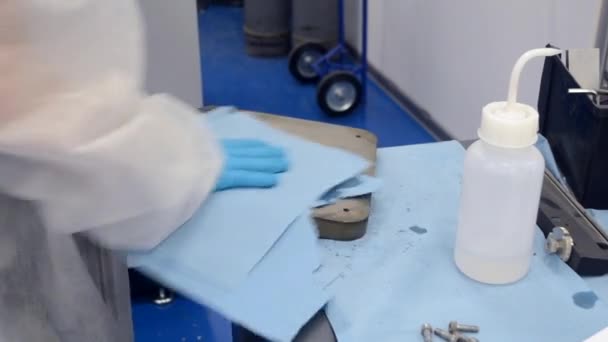 Werknemer in wit beschermingspak en blauwe beschermingshandschoenen Reiniging van metalen deel — Stockvideo