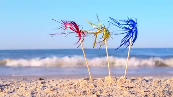 Drie felgekleurde cocktaildecoraties staan in het zand bij de zee close-up. — Stockvideo