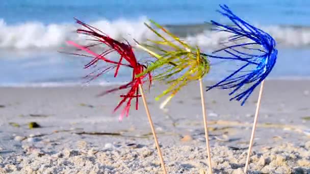 Three bright shiny colored cocktail decorations stand in sand near sea close-up. — Vídeo de Stock