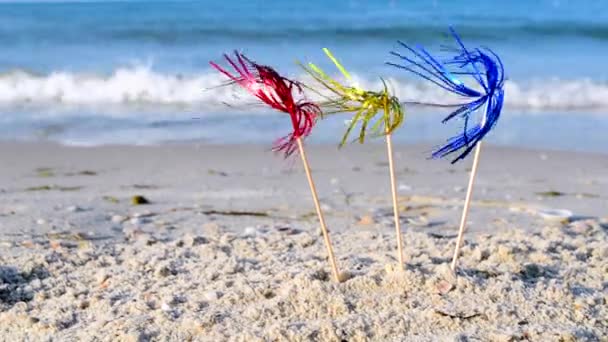 Trzy jasne błyszczące kolorowe dekoracje koktajlowe stoją w piasku w pobliżu morza zbliżenie. — Wideo stockowe