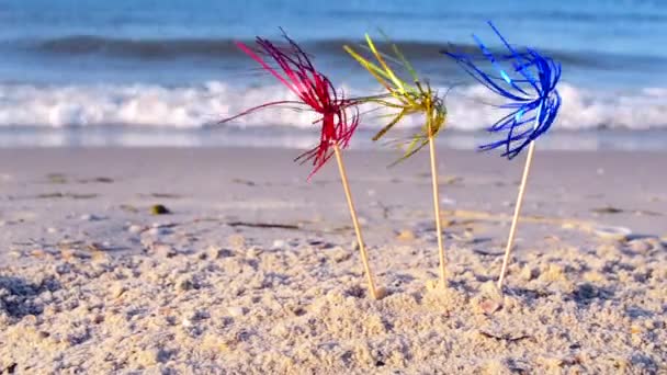 Three bright shiny colored cocktail decorations stand in sand near sea close-up. — Vídeo de Stock